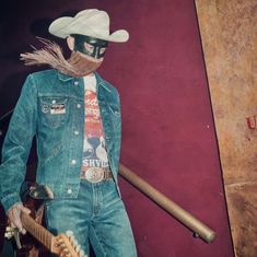 a man wearing a cowboy hat and holding a guitar in front of a red wall