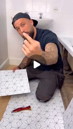 a man sitting on the floor in front of a bathroom sink and looking at something