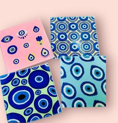 three notebooks with blue and pink designs on them, one in the shape of an eye