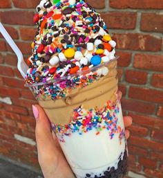 a person holding an ice cream sundae with sprinkles and toppings