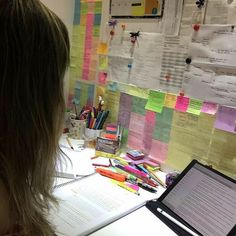 a woman sitting at a desk with a laptop computer in front of her and papers on the wall behind her