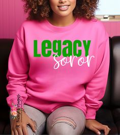 a woman sitting on a couch wearing a pink sweatshirt with the words legacy soror