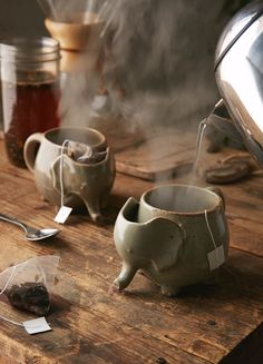 an elephant shaped tea pot is sitting on a table next to other cups and spoons