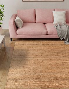 a living room with a pink couch, rug and potted plant on the floor