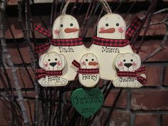 three snowmen are hanging from a tree in front of a brick wall with a green heart