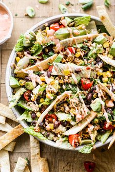 a bowl filled with taco salad and tortilla chips on top of a wooden table