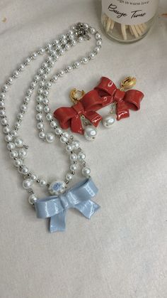 two necklaces with bows and pearls sitting on a table next to a jar of candy