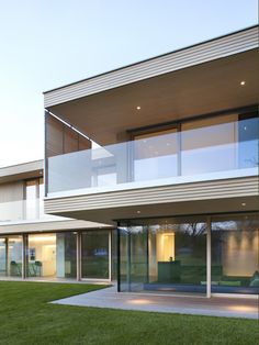 a modern house with glass walls and sliding doors on the outside, grass lawn in front