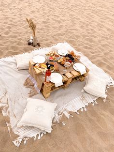 a picnic table set up on the beach with plates and drinks in front of it