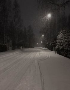 a snow covered street at night with the lights on and trees in the background,