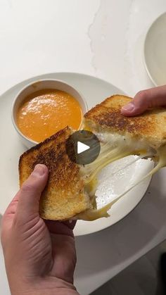 someone is eating a grilled cheese sandwich with butter and tomato soup on the side