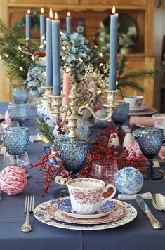 a table set with blue and white dishes, silverware, candles and other decorations