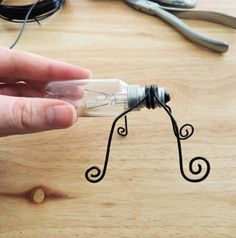 a hand holding a small light bulb with wire attached to it on top of a wooden table