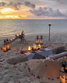 a table set up on the beach with candles and flowers