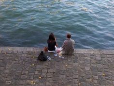 two people sitting on the edge of a river