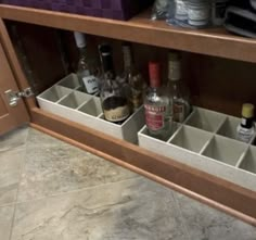 an open cabinet filled with liquor bottles on top of a tiled floor next to a counter