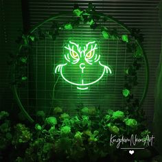 a green neon sign with a cat's face on it in front of some plants