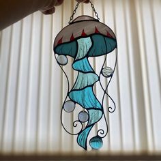 a hand holding a stained glass hanging lamp in the shape of a jellyfish on a chain