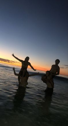 three people in the water at sunset with their arms spread out and hands extended up