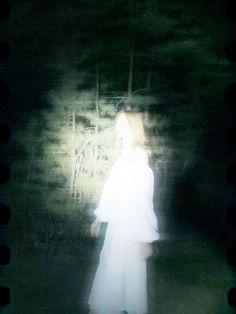 a blurry photo of a woman in a white dress walking through the woods at night