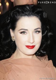 a close up of a person wearing a dress and red lipstick with people in the background