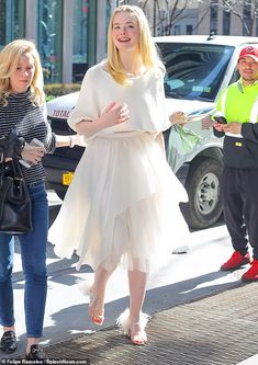 a woman in a white dress is walking down the street with two other people behind her