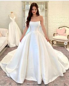 a woman standing in front of a dress on display at a bridal shop wearing a white wedding gown