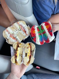 two people holding sandwiches in their hands while sitting in the back seat of a car