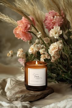 a candle sitting on top of a wooden table next to some flowers and pamy grass