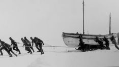 a group of men pulling a boat on top of snow covered ground