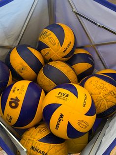 a bunch of yellow and blue volleyballs are in a plastic container on the floor