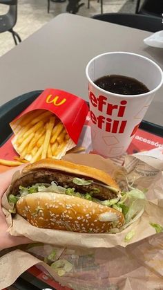 a person holding a sandwich and french fries on a tray with a cup of coffee