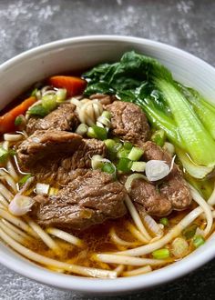 a white bowl filled with meat and noodles next to vegetables on top of a table