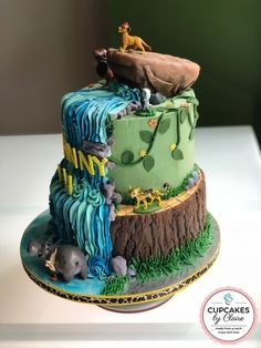 a cake that is decorated with animals and trees on top of the cake, sitting on a table