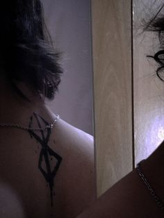 a woman's back with a cross tattoo on her left shoulder, and a mirror in the background