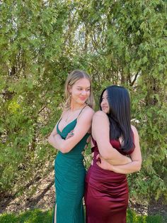 two women standing next to each other in front of trees and bushes with their arms around each other