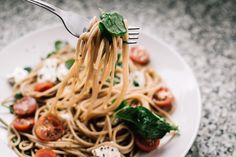 a fork full of pasta with tomatoes and spinach on it is being held up to the camera