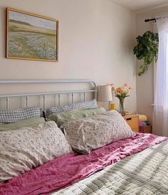 a bed with pink sheets and pillows next to a painting on the wall above it