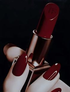 a woman's hand with red and white nails holding a lipstick in her left hand