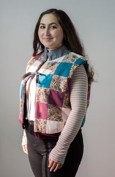 a woman standing with her hands on her hips wearing a multicolored vest and black pants