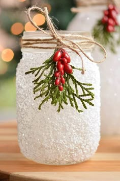 a mason jar filled with white snow and red berries on top of a wooden table