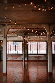 an empty room with wooden floors and string lights hanging from the ceiling in front of large windows