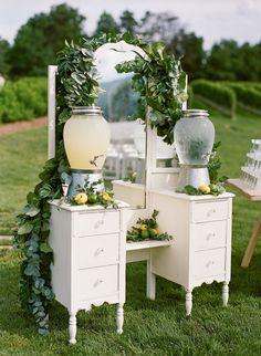 a white dresser sitting on top of a lush green field next to a tall mirror