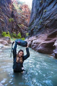 a woman is wading through the water in a canyon