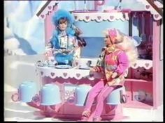 two barbie dolls are sitting in front of a pink toy house and one is talking to the other