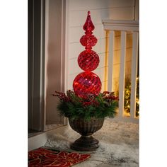 a christmas decoration with red balls and greenery in a urn on the front porch