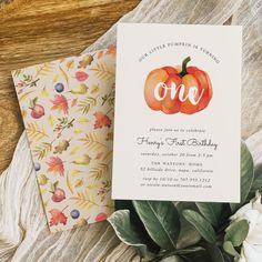 an orange pumpkin is on top of a card next to some flowers and greenery