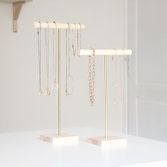 two gold jewelry stands on top of a white table