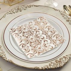 a white and gold plate topped with a napkin on top of a table next to utensils