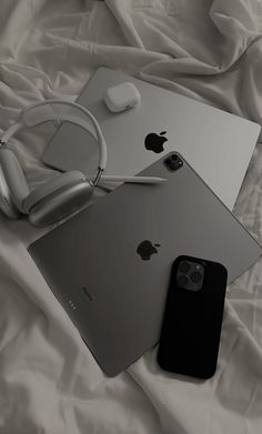 an apple laptop, headphones and iphone on a bed